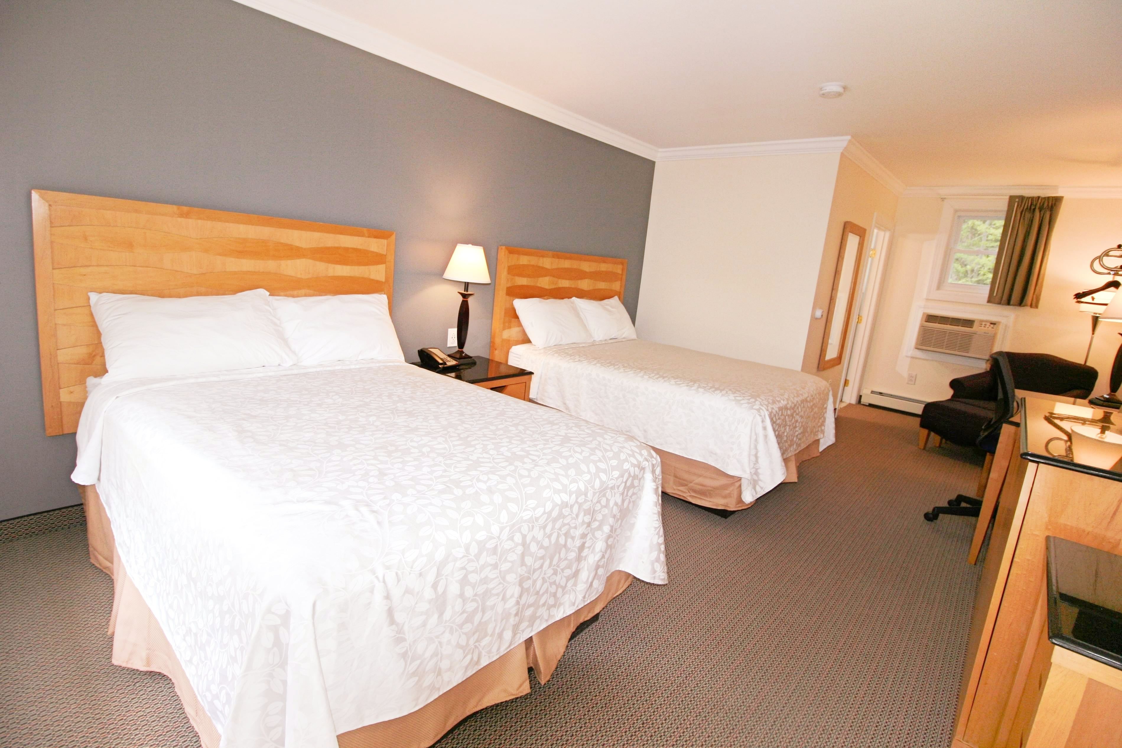Une chambre d’hôtel avec deux lits, un bureau avec une chaise, une lampe et un appareil de climatisation.