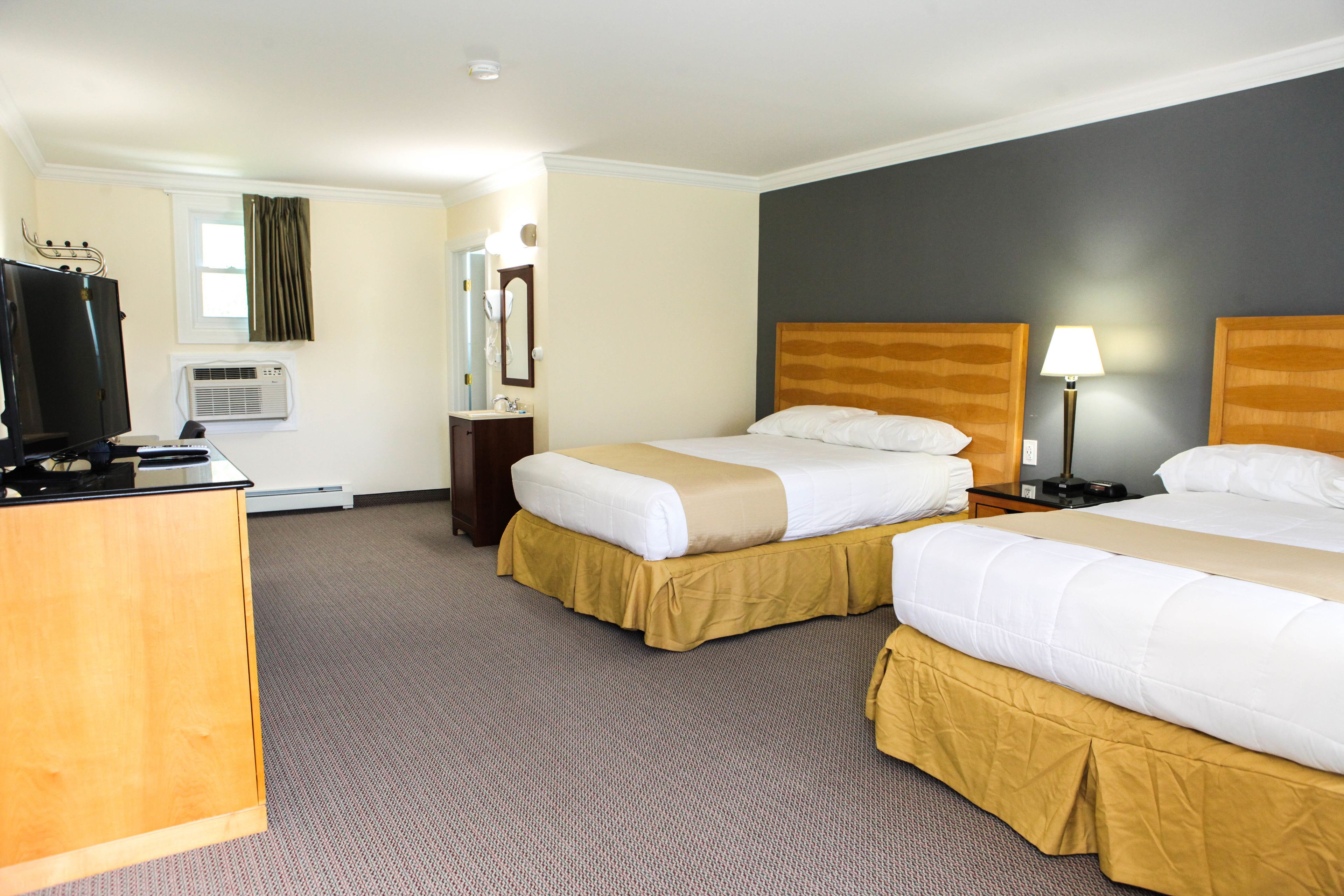 A hotel room with two beds, a desk, a television, a mirror, and a window with curtains.