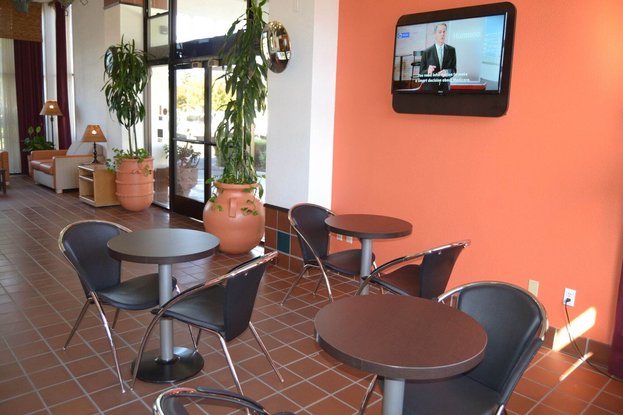 Un'area salotto con tavoli e sedie, uno schermo televisivo che mostra un telegiornale e piante in vaso.
