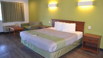 A hotel room with a large bed, two bedside tables, a chair, a desk, and a window with curtains.