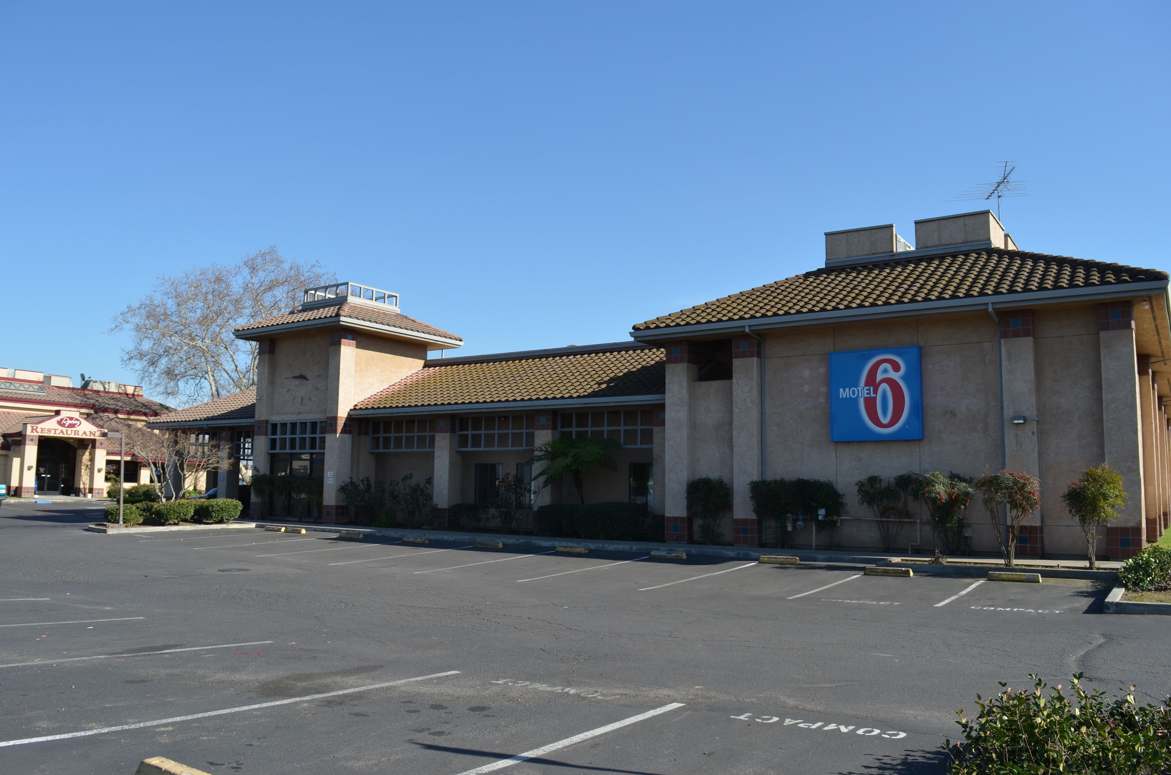 A motel with a large sign, a parking lot, and a restaurant in the background.