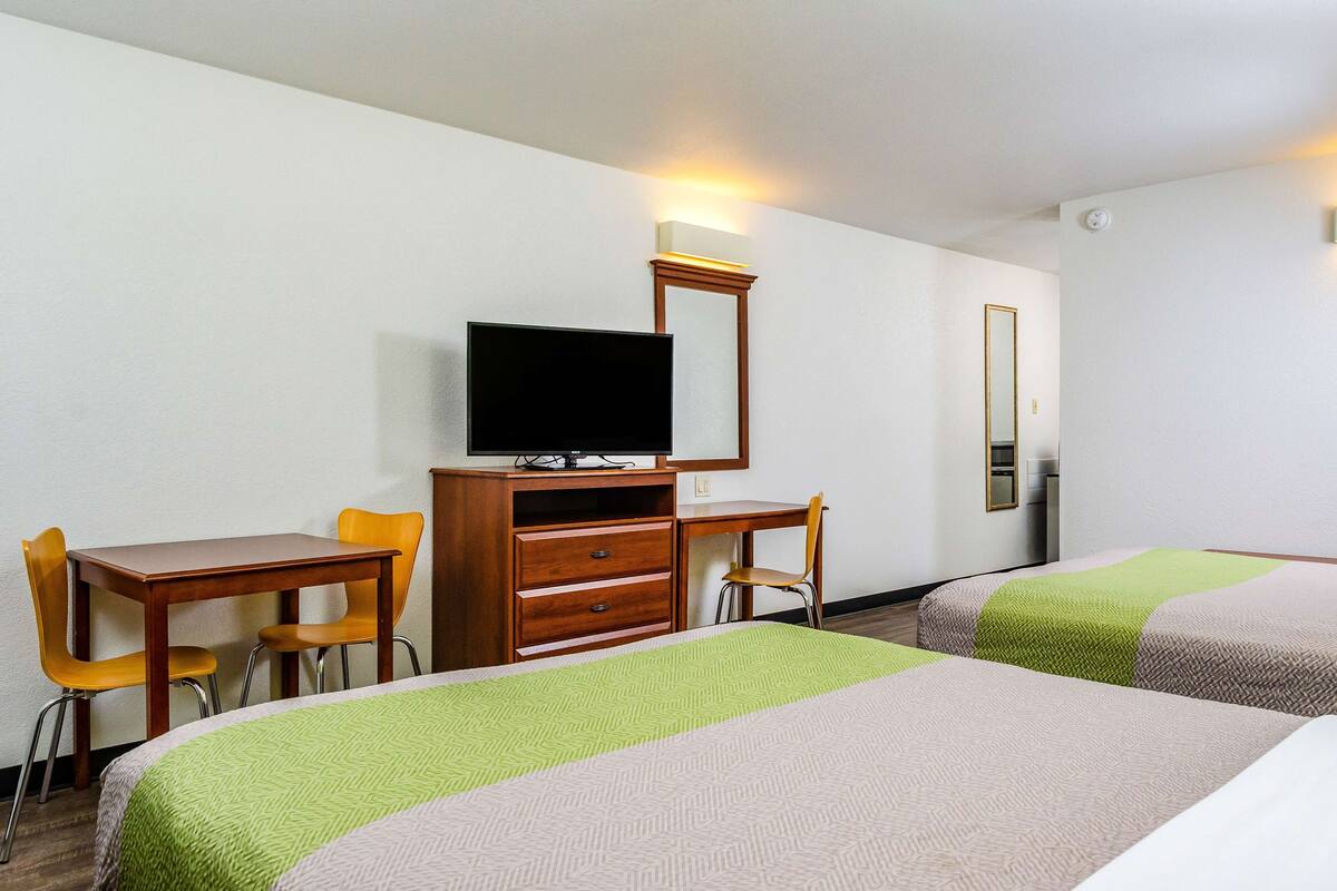 A hotel room with two beds, a desk, a chair, a television, and a mirror.