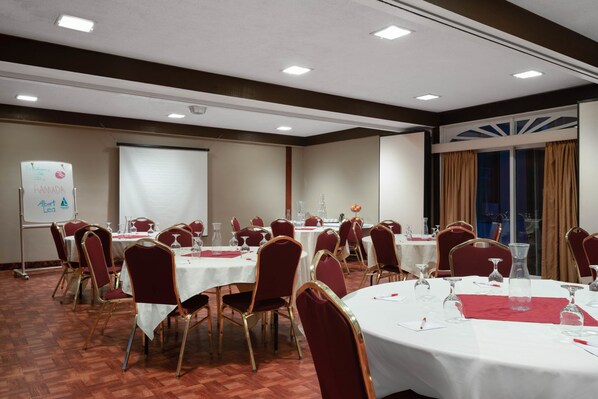 Un salón de conferencias con varias mesas redondas, sillas rojas y una pizarra.