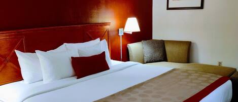 Habitación de hotel con una cama grande, cabecera de madera, lámpara de noche y un cuadro en la pared.