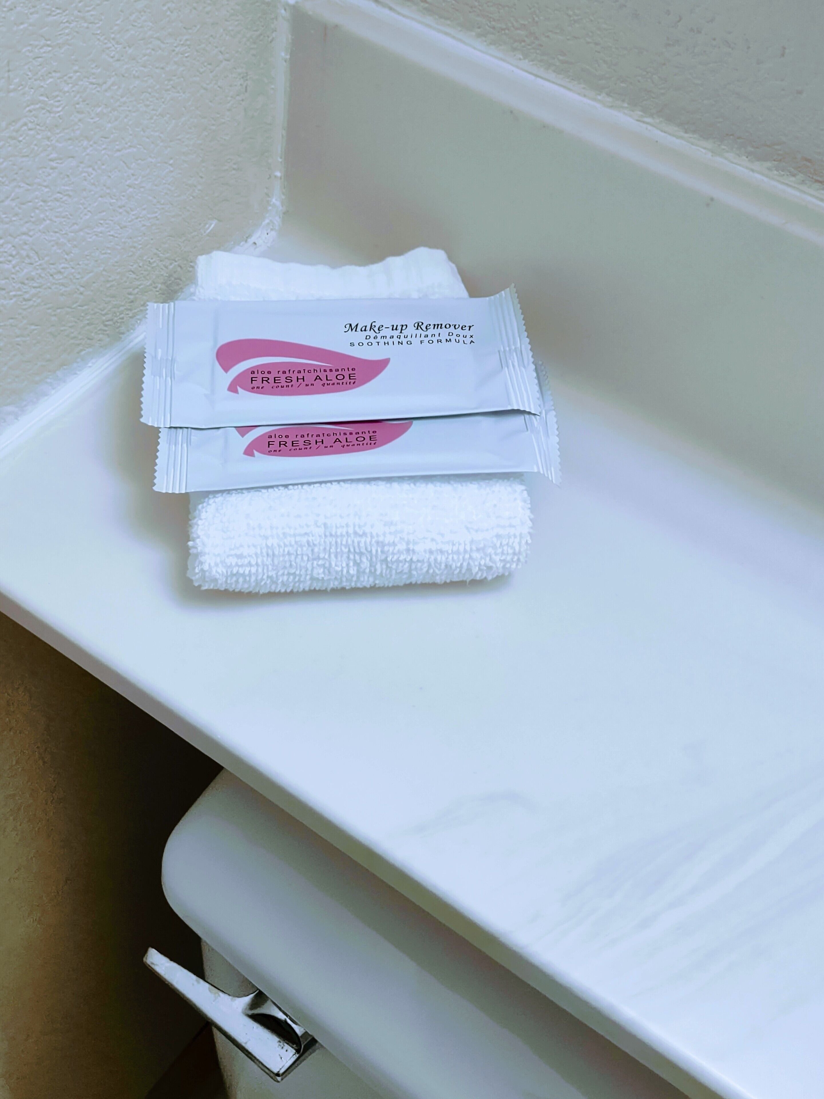 A bathroom with a white sink, a towel, and two packets of aloe vera gel.