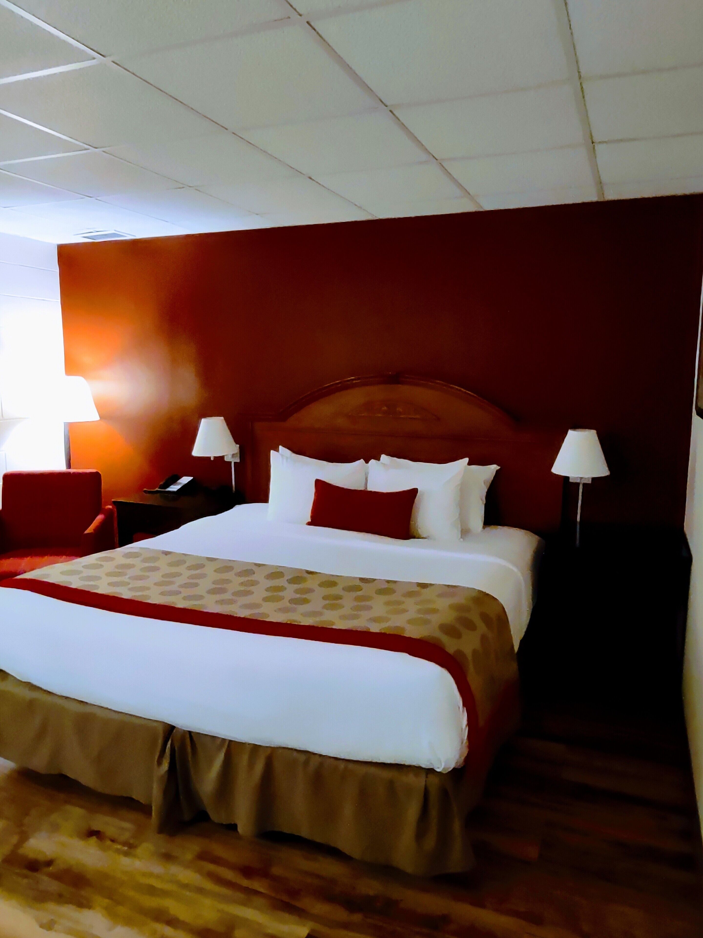 Una habitación de hotel con una cama grande, dos mesitas de noche, una pared roja y suelo de madera.
