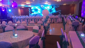 Un salón de banquetes con mesas y sillas redondas, cada una decorada con manteles blancos y cintas verdes.