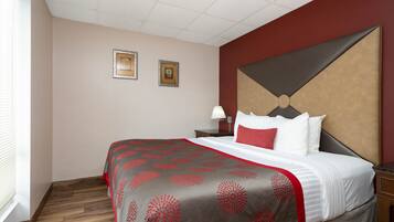 Een hotelkamer met een groot bed, een nachtkastje, twee ingelijste foto's aan de muur en een raam met luxaflex.