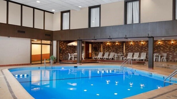 Una piscina interior con piso de baldosas, rodeada de sillas de descanso y un muro de ladrillo.