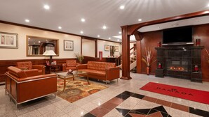 Un vestíbulo de hotel con sofás de cuero, una mesa de centro, una chimenea y una alfombra roja con la inscripción 'RAMADA'.