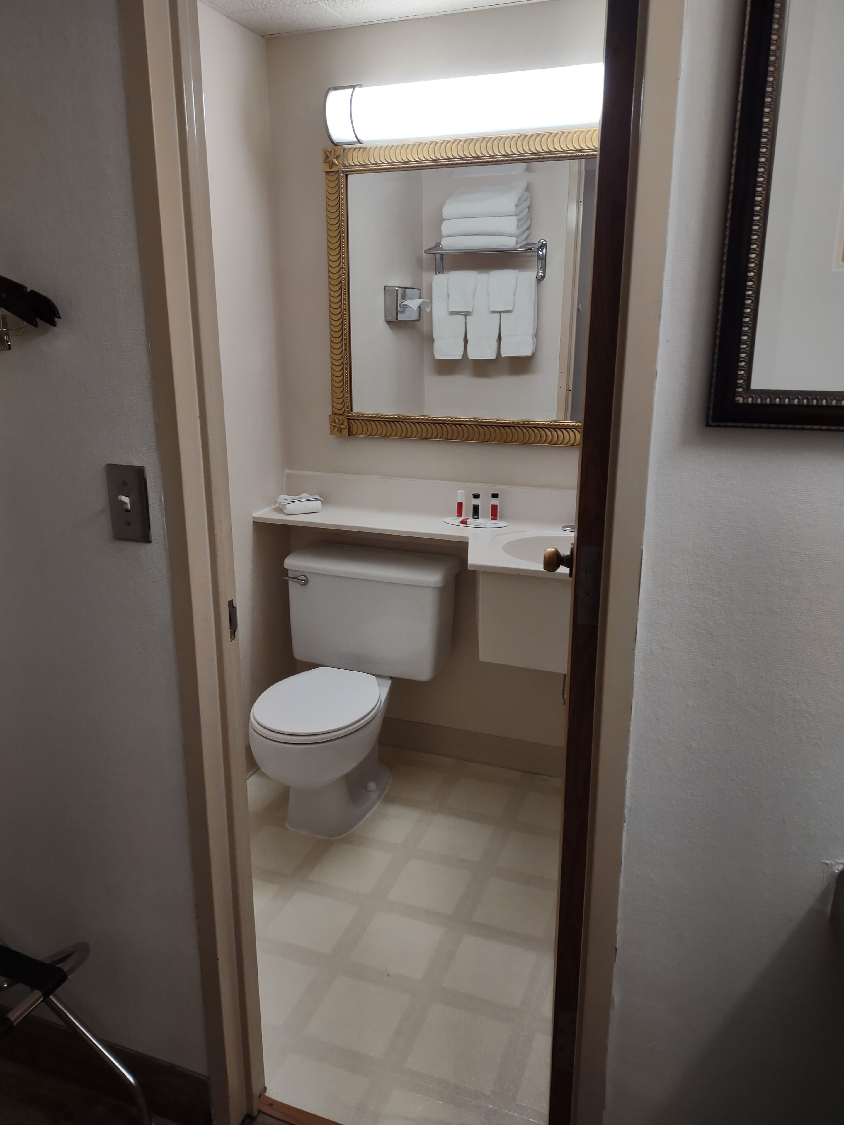 A bathroom with a toilet, sink, and mirror. There is a towel rack with folded towels above the mirror.