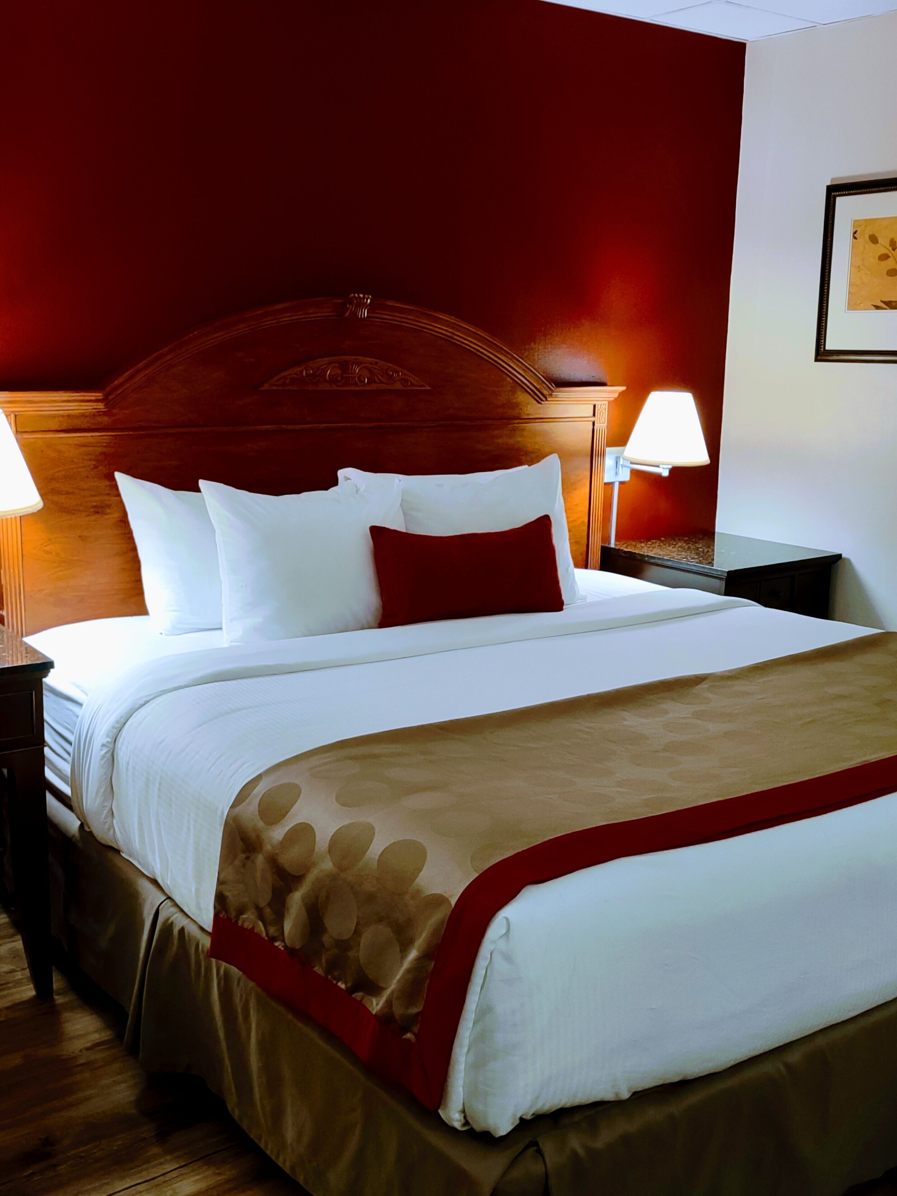 A neatly made bed with white and red bedding, a wooden headboard, and two bedside lamps.
