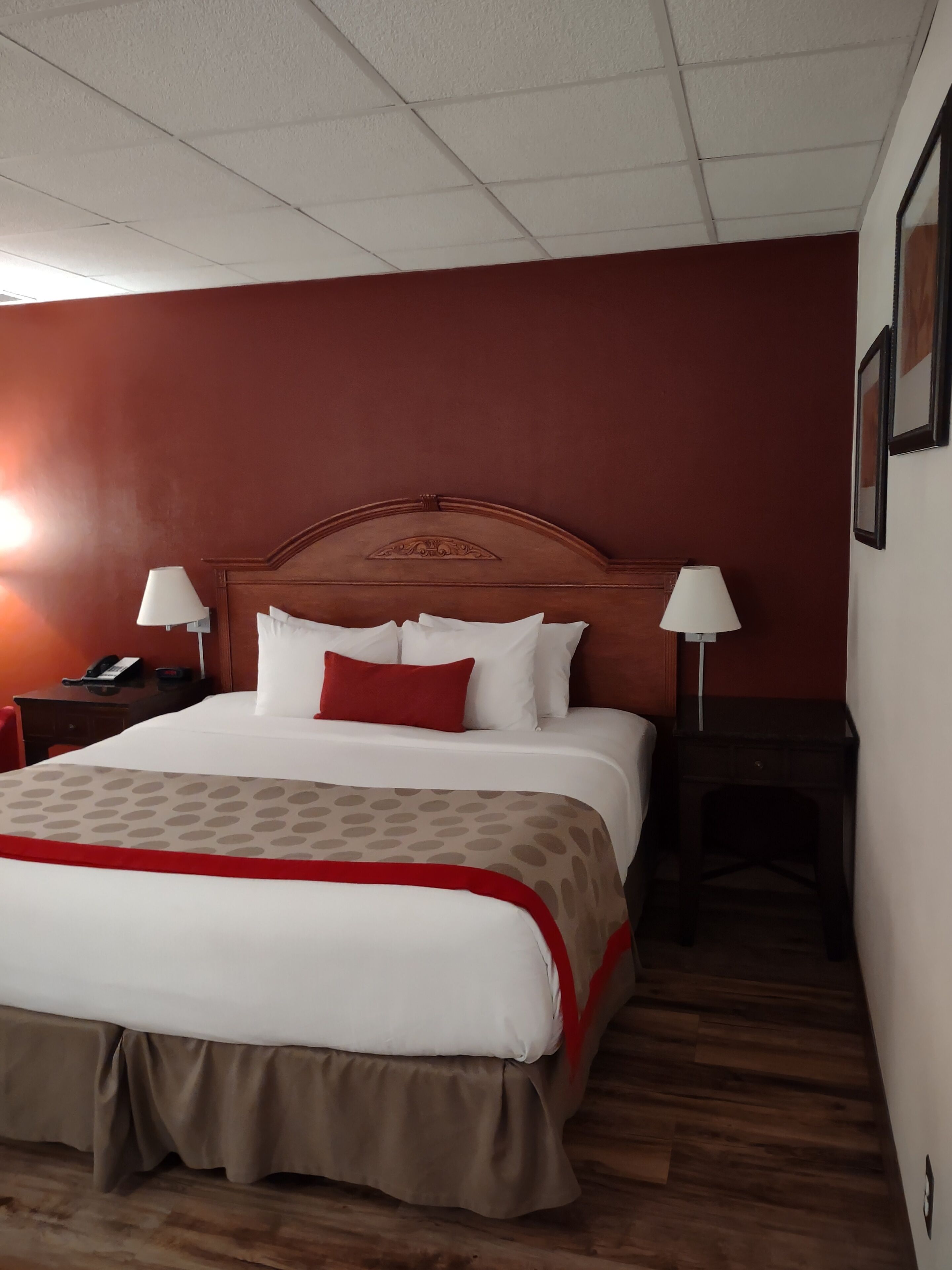 Habitación de hotel con una cama grande, dos mesitas de noche con lámparas, suelo de madera y paredes rojas.