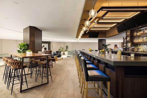 A modern bar area with a long counter, bar stools, and a variety of bottles.