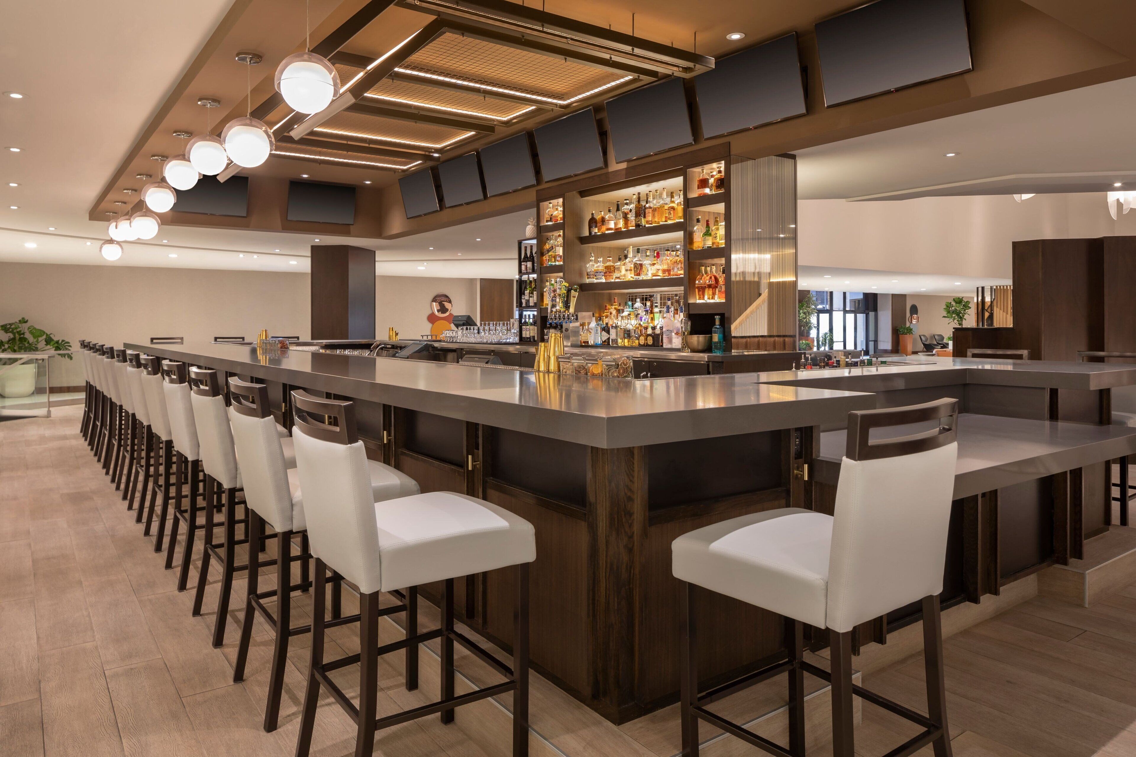 A modern bar area with a long counter, multiple stools, and a well-stocked bar.