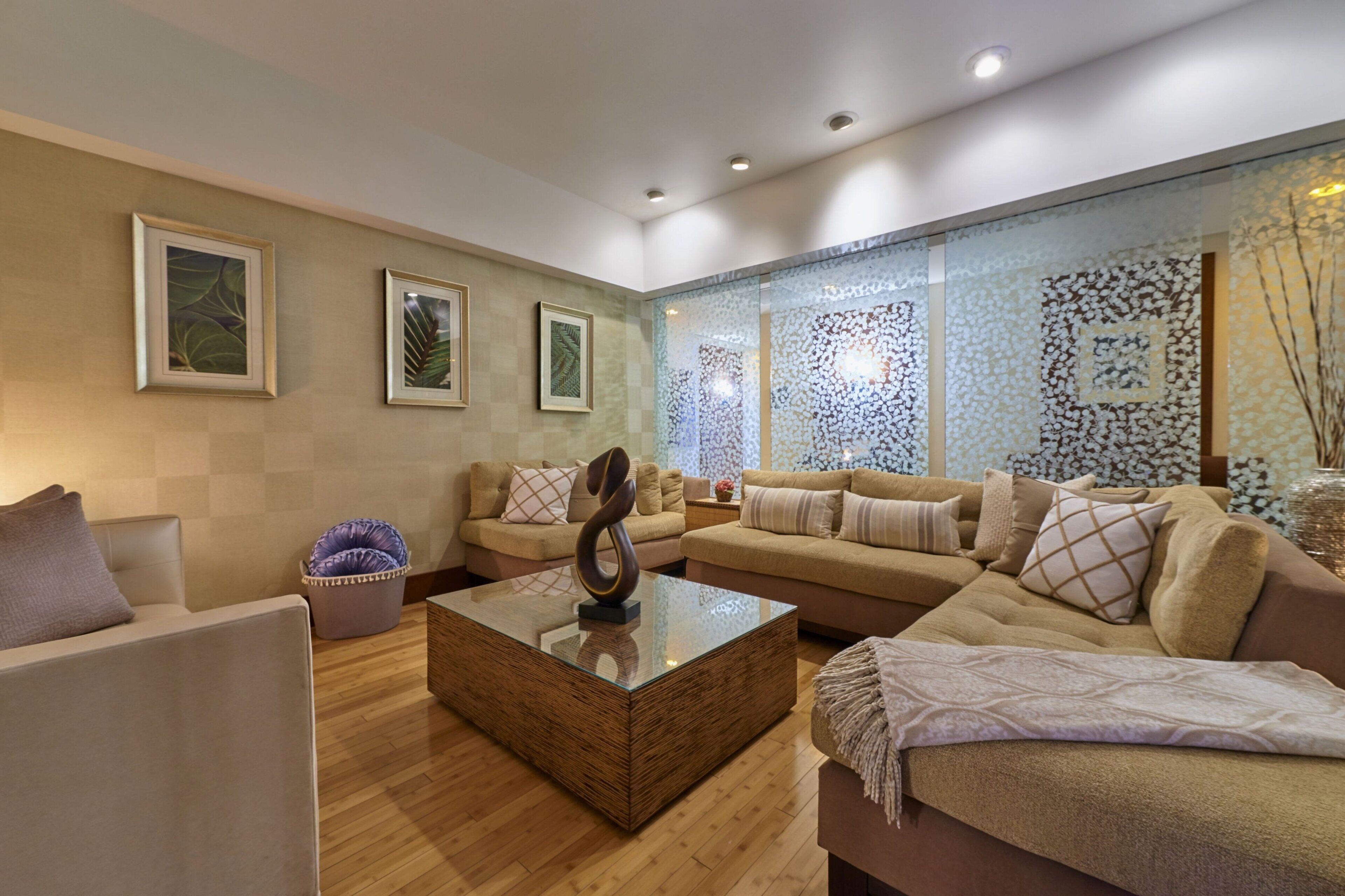 A modern living room with a large sectional sofa, a glass coffee table, and a decorative wall panel.