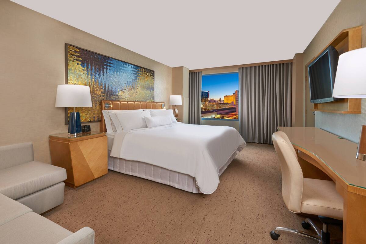 Una habitación de hotel con cama, escritorio, silla, televisor y un cuadro en la pared.