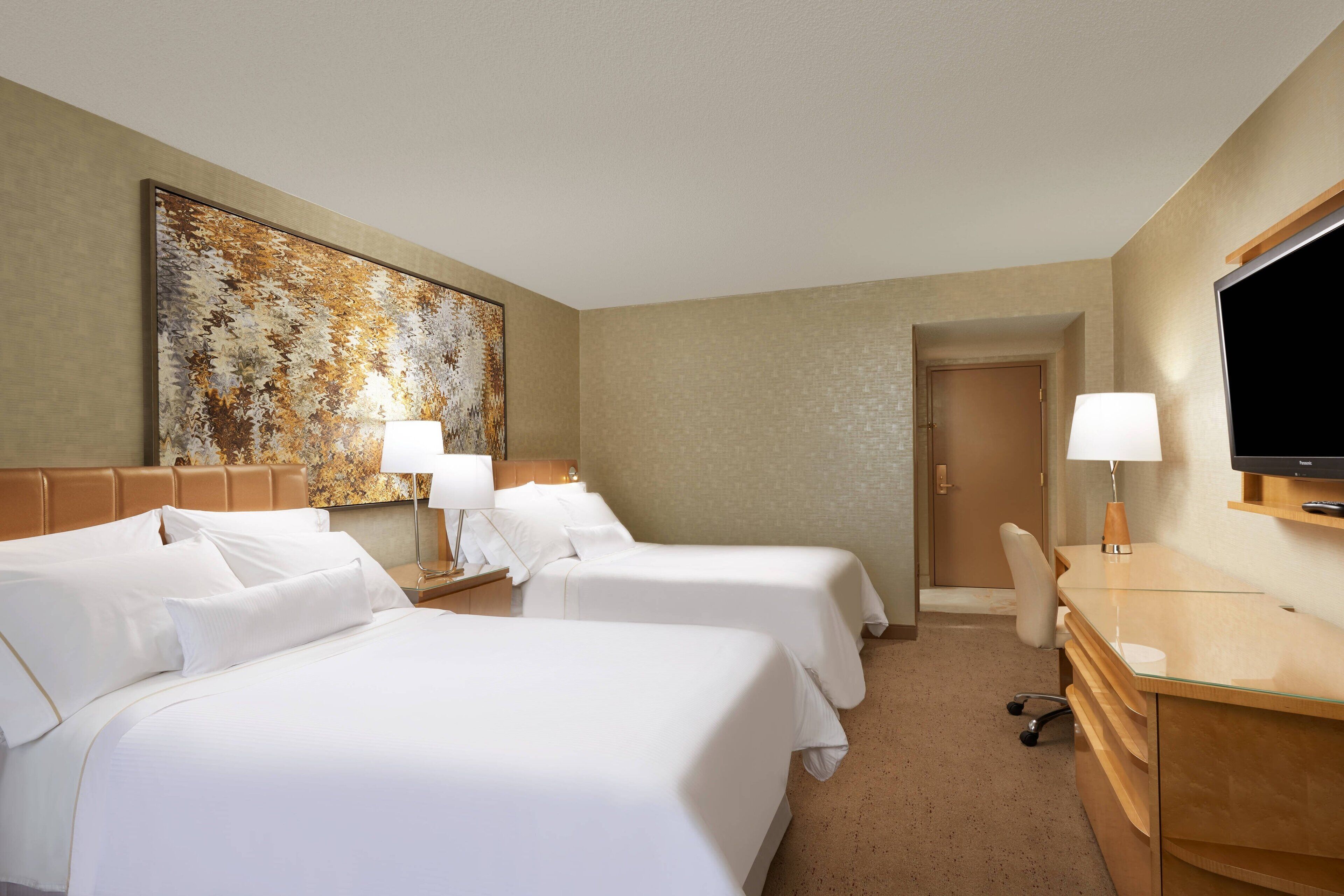 A hotel room with two beds, a desk, a television, and a large abstract painting on the wall.