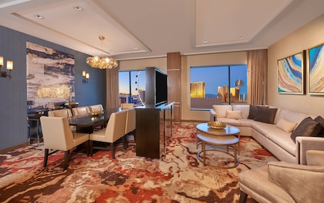 A modern hotel room with a dining area, a sofa, and a large window with a city view.