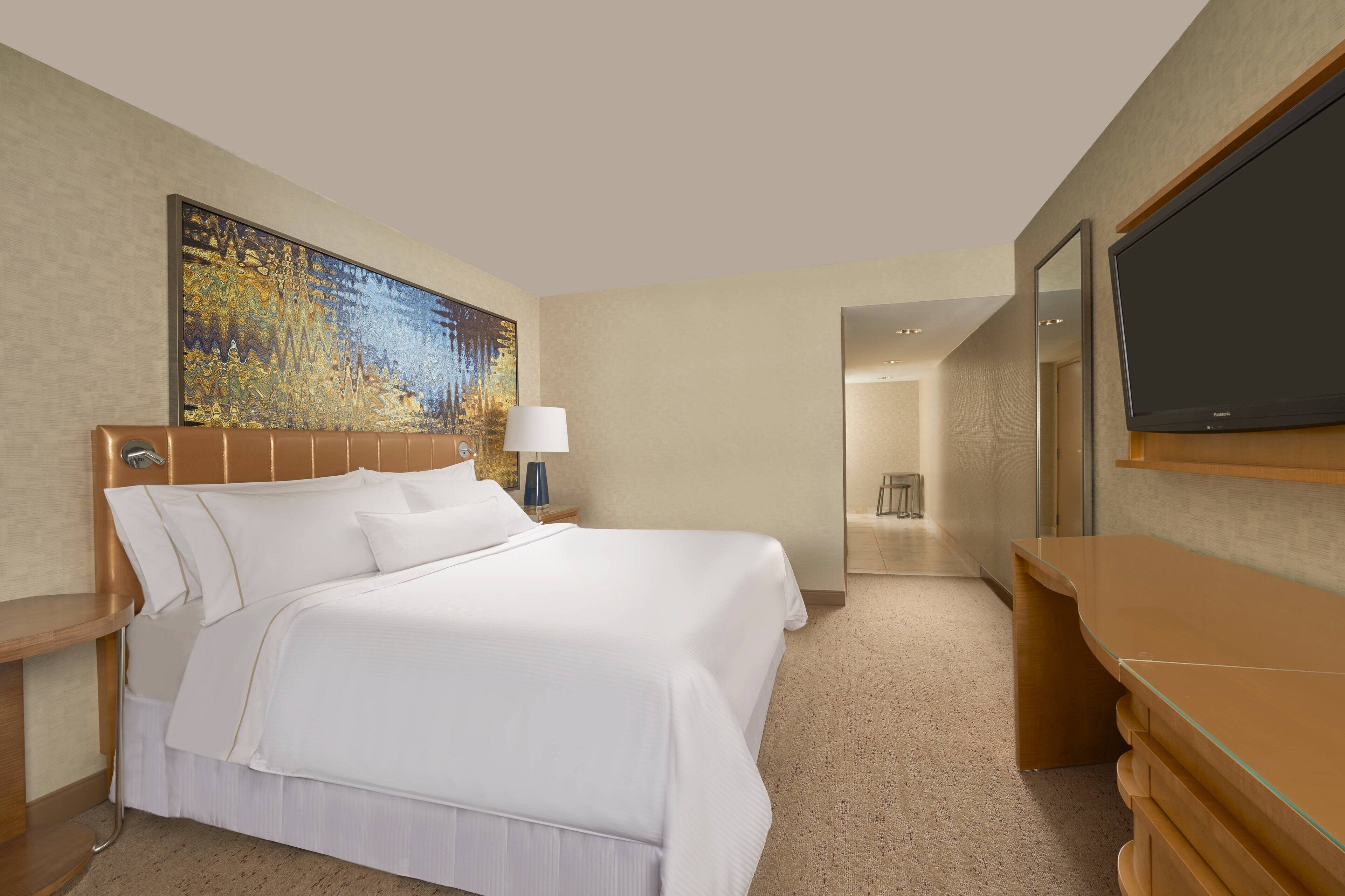 Ein Hotelzimmer mit einem großen Bett, einem Fernseher, einem Schreibtisch und einem Gemälde an der Wand.