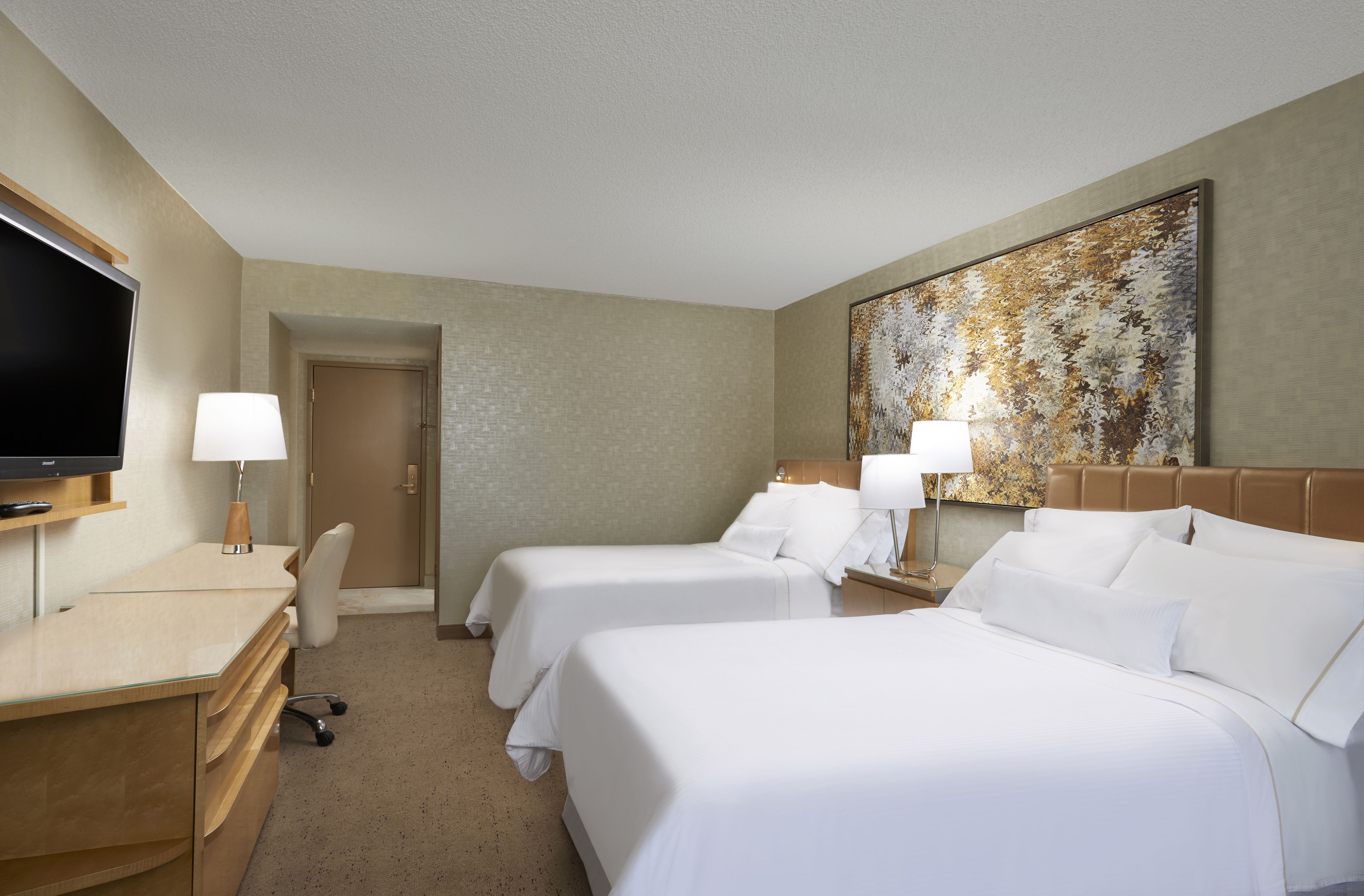 A hotel room with two beds, a desk, a TV, and a painting on the wall.