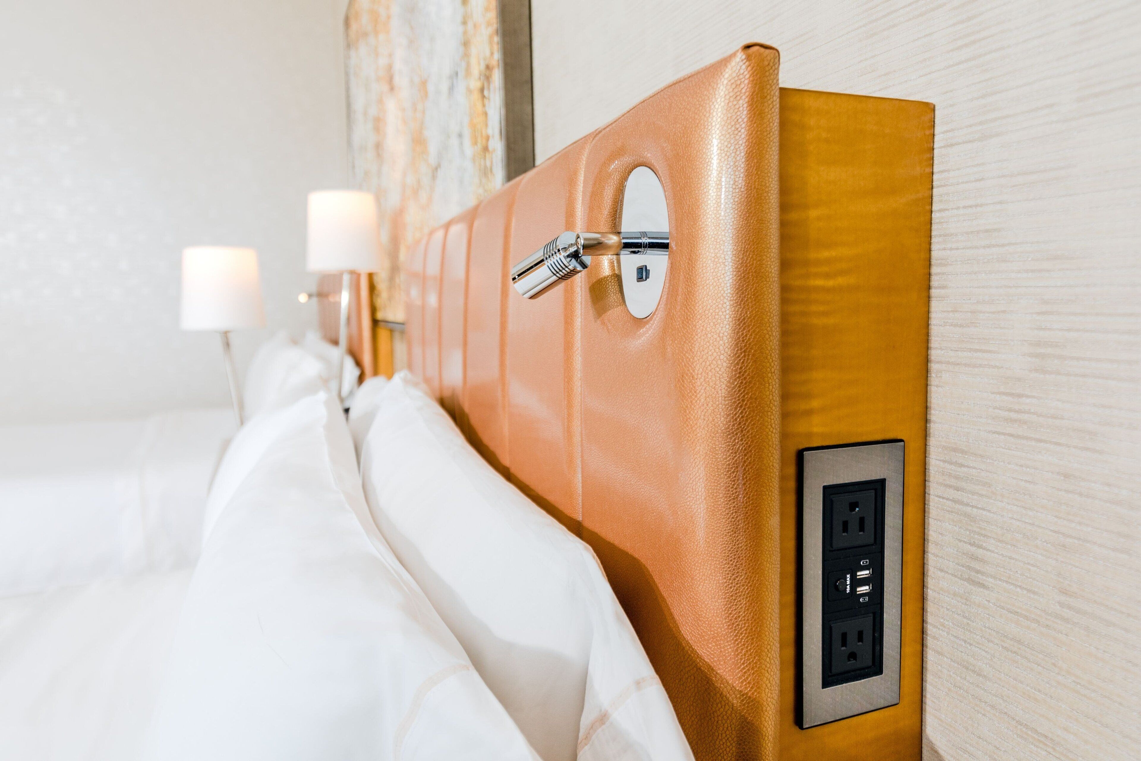 A hotel room with a wooden headboard, a bed with white linens, and a wall-mounted power outlet.