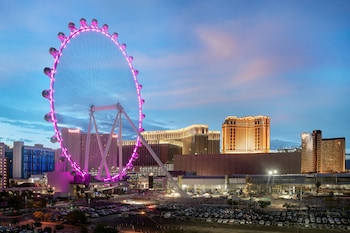 A hotel with a prominent Ferris wheel in the background, a parking lot, and a view of the surrounding cityscape. at The Westin Las Vegas Hotel & Spa
