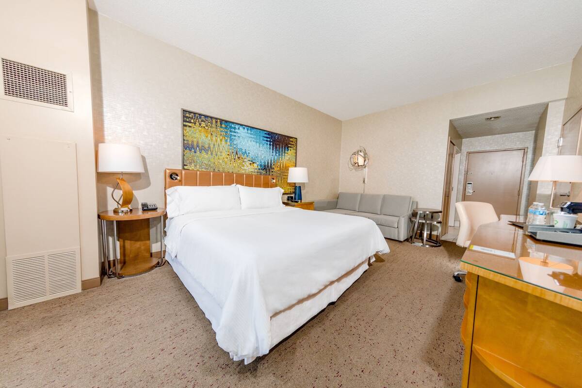 Una habitación de hotel con una cama grande, un escritorio, una silla, un sofá y un cuadro en la pared.