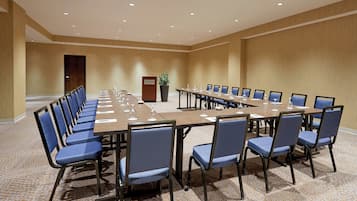 Una sala de conferencias con una larga mesa y sillas, un atril y una planta en maceta.