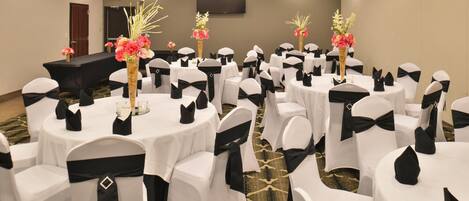 A conference room with round tables, white chairs with black sashes, and floral centerpieces.