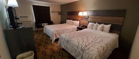 Ein Hotelzimmer mit zwei Betten, einem Schreibtisch, einem Stuhl, einer Lampe und einem Mülleimer.