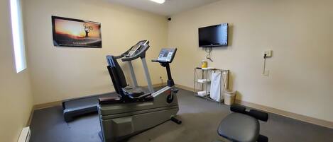 A fitness room with treadmills, a chair, a TV, and a poster on the wall.