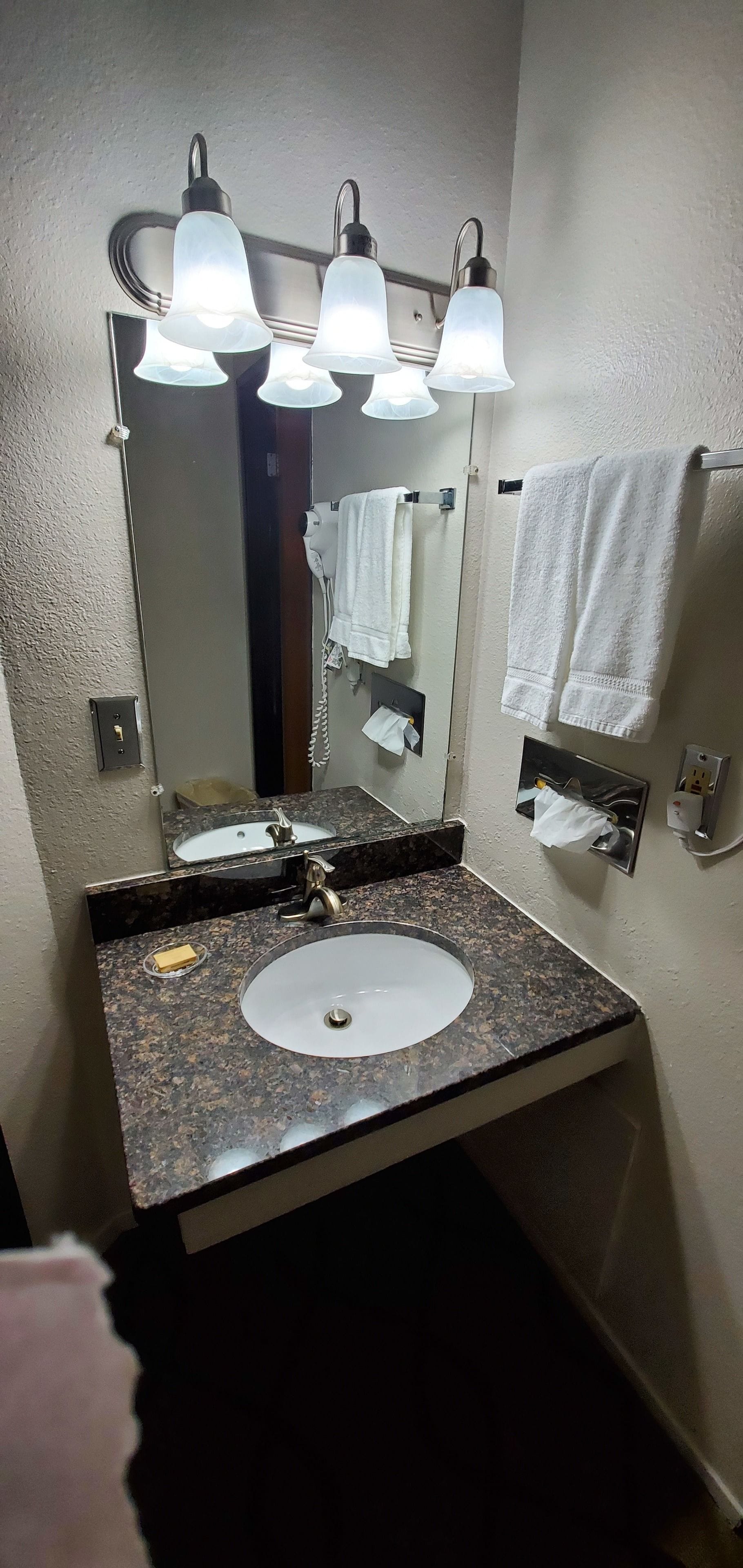Un baño con lavamanos de encimera de granito, un espejo y tres luces empotradas.