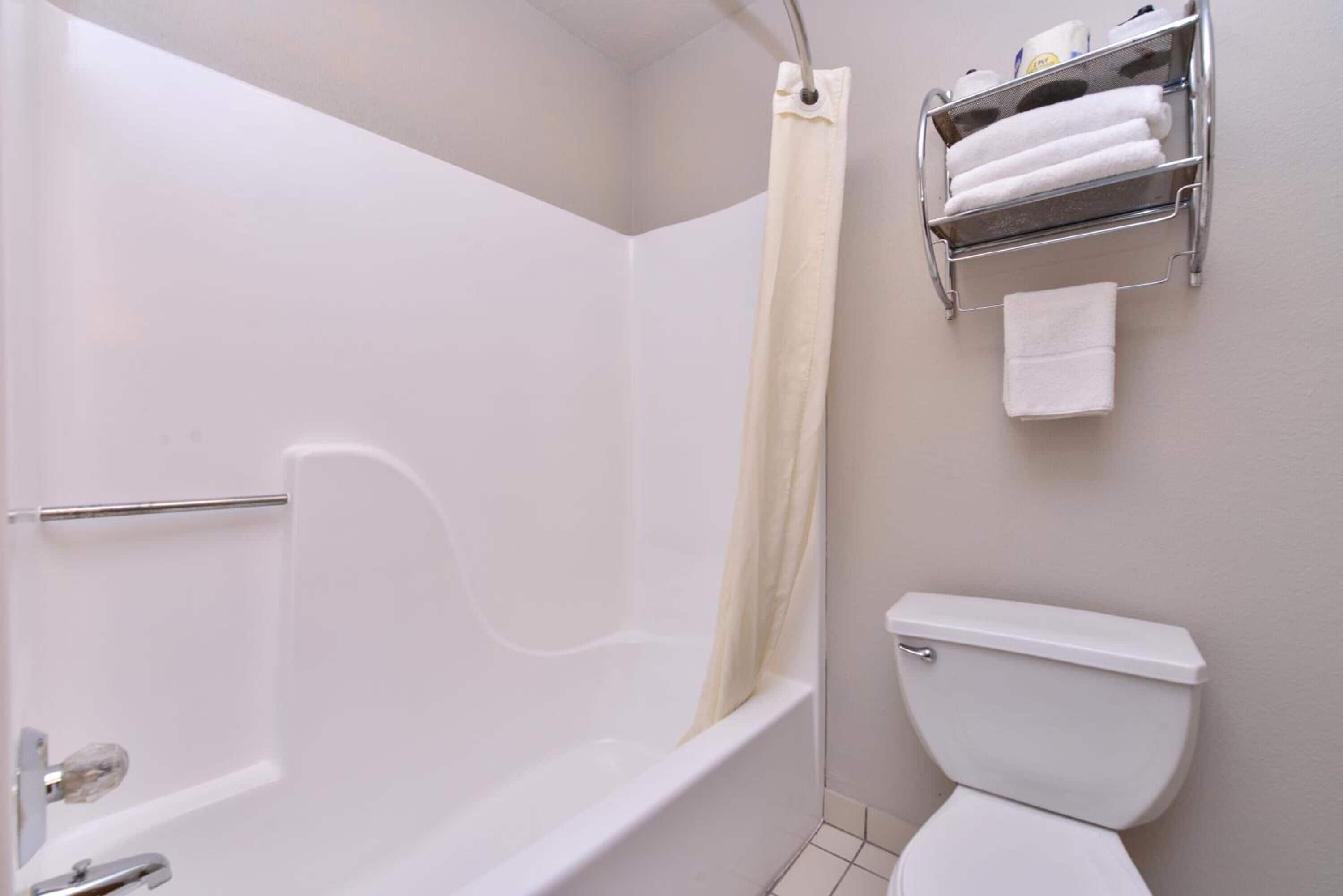 A bathroom with a bathtub, toilet, and a towel rack with towels.