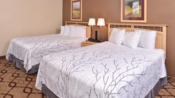 Habitación de hotel con dos camas, cada una con cubrecama estampado con ramas de árbol, una mesita de noche con lámpara y dos cuadros en la pared.