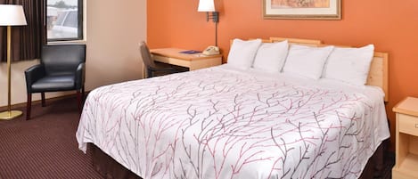 A hotel room with a large bed, a desk, a chair, a lamp, and a painting on the wall.