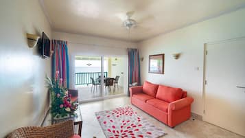 A living room with a red sofa, a wicker chair, a glass table, a decorative rug, and a ceiling fan.
