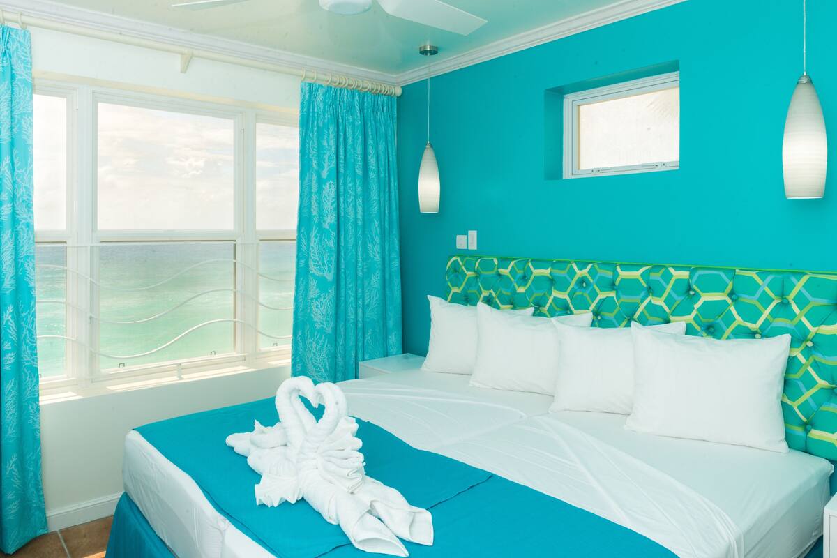 Una habitación de hotel con una cama, una ventana con cortinas, un cabecero con diseño geométrico y una lámpara de pared.