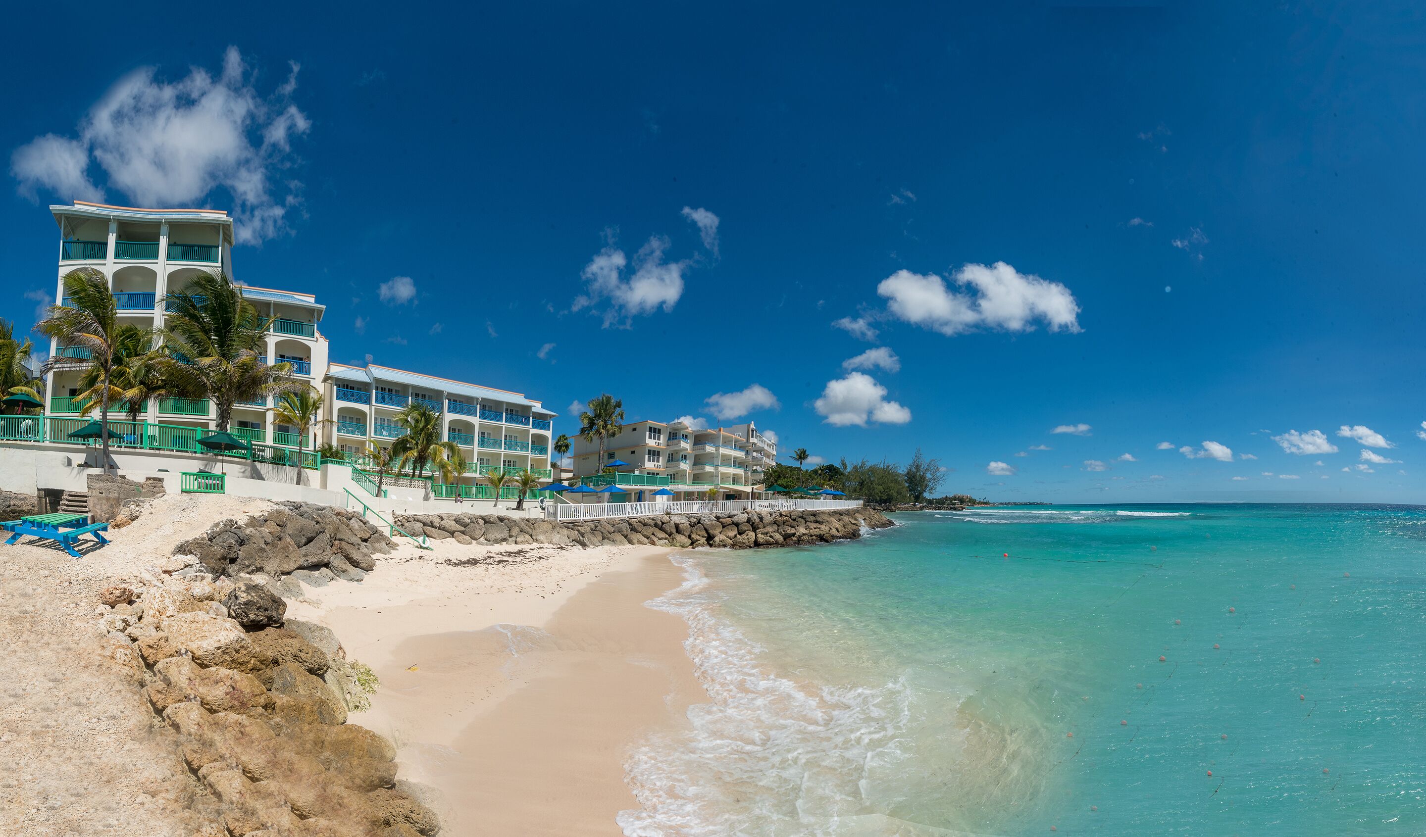 A beachfront hotel with multiple balconies, a sandy beach, and clear turquoise waters.