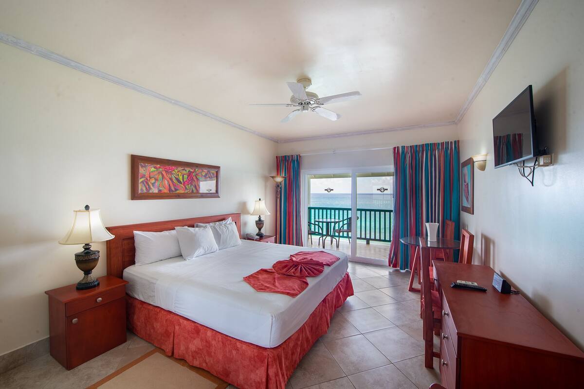 Una habitación de hotel con cama, escritorio, televisor y balcón con cortinas.