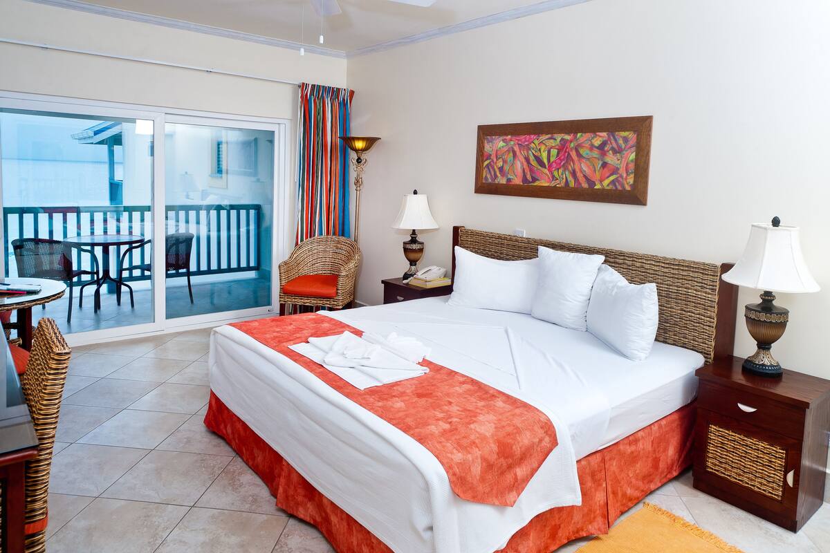 Habitación de hotel con una cama grande, un balcón con mesa y sillas, y un cuadro en la pared.