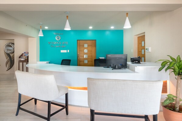 A reception area with a turquoise wall, a wooden door, and a reception desk. There are two white chairs in front of the desk. - Rostrevor Hotel (St. Lawrence Gap)
