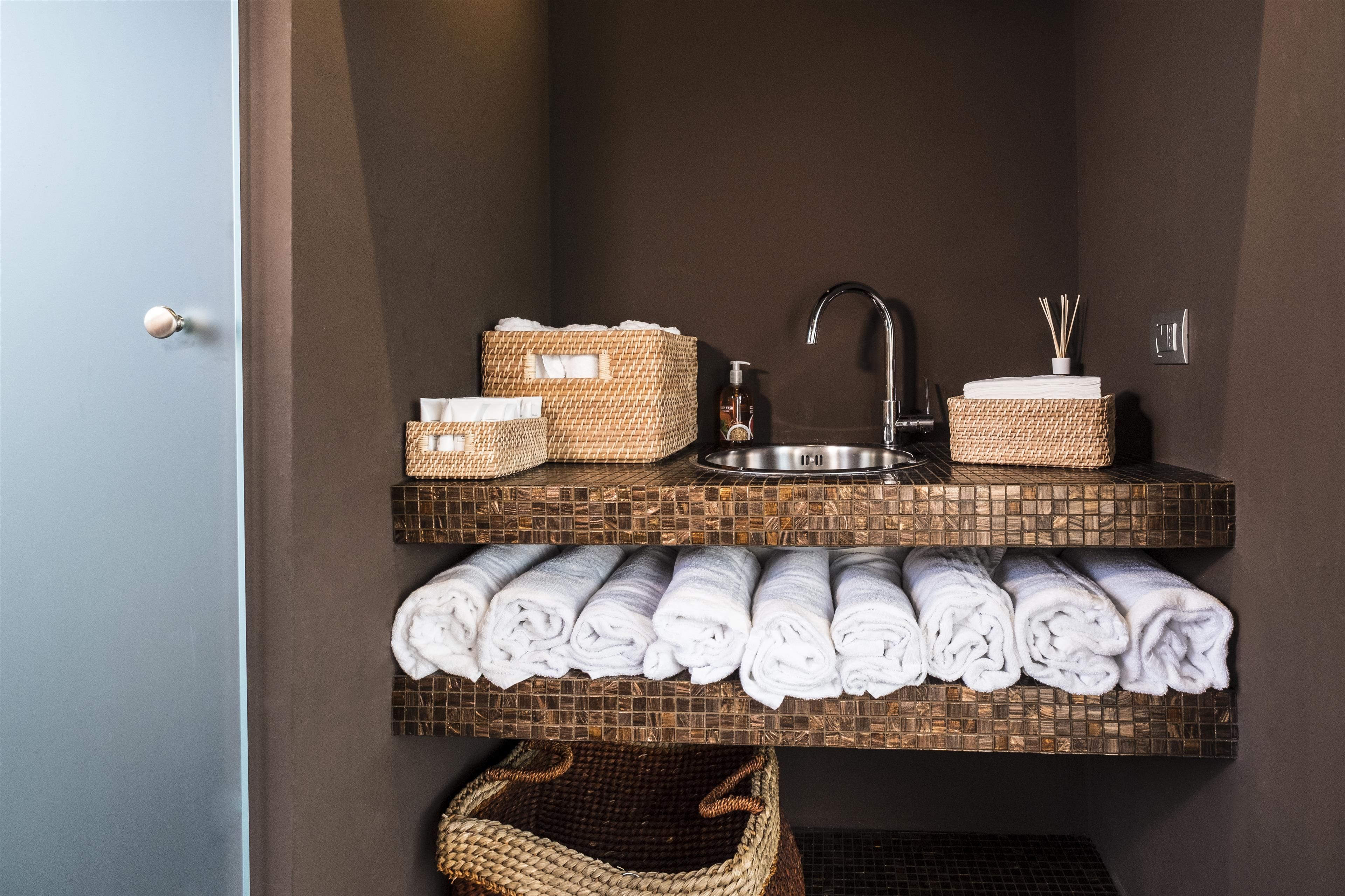 A bathroom with a dark brown wall, a sink with a faucet, and shelves holding towels and baskets.