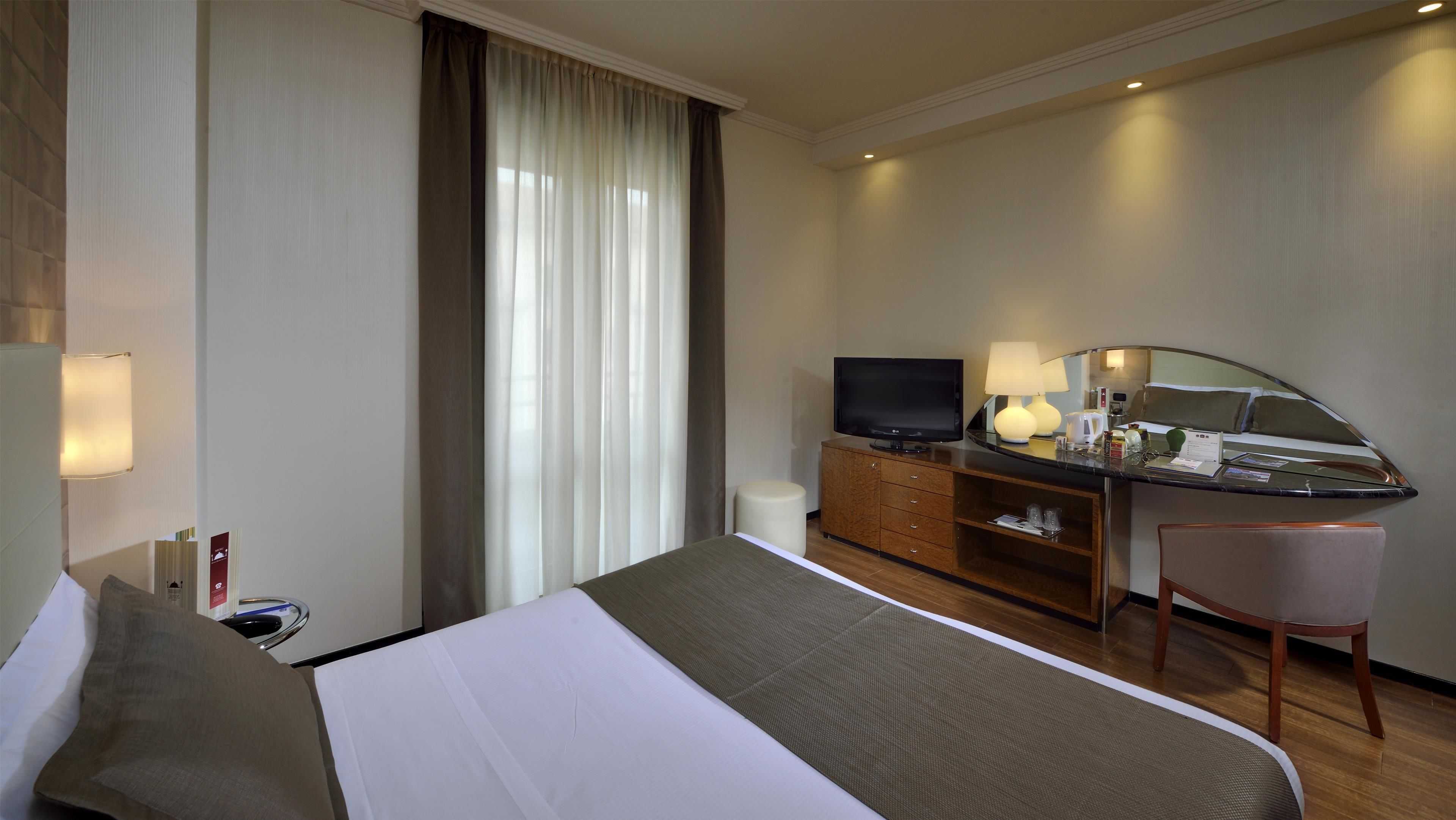 A hotel room with a bed, a desk, a television, a mirror, and a chair.