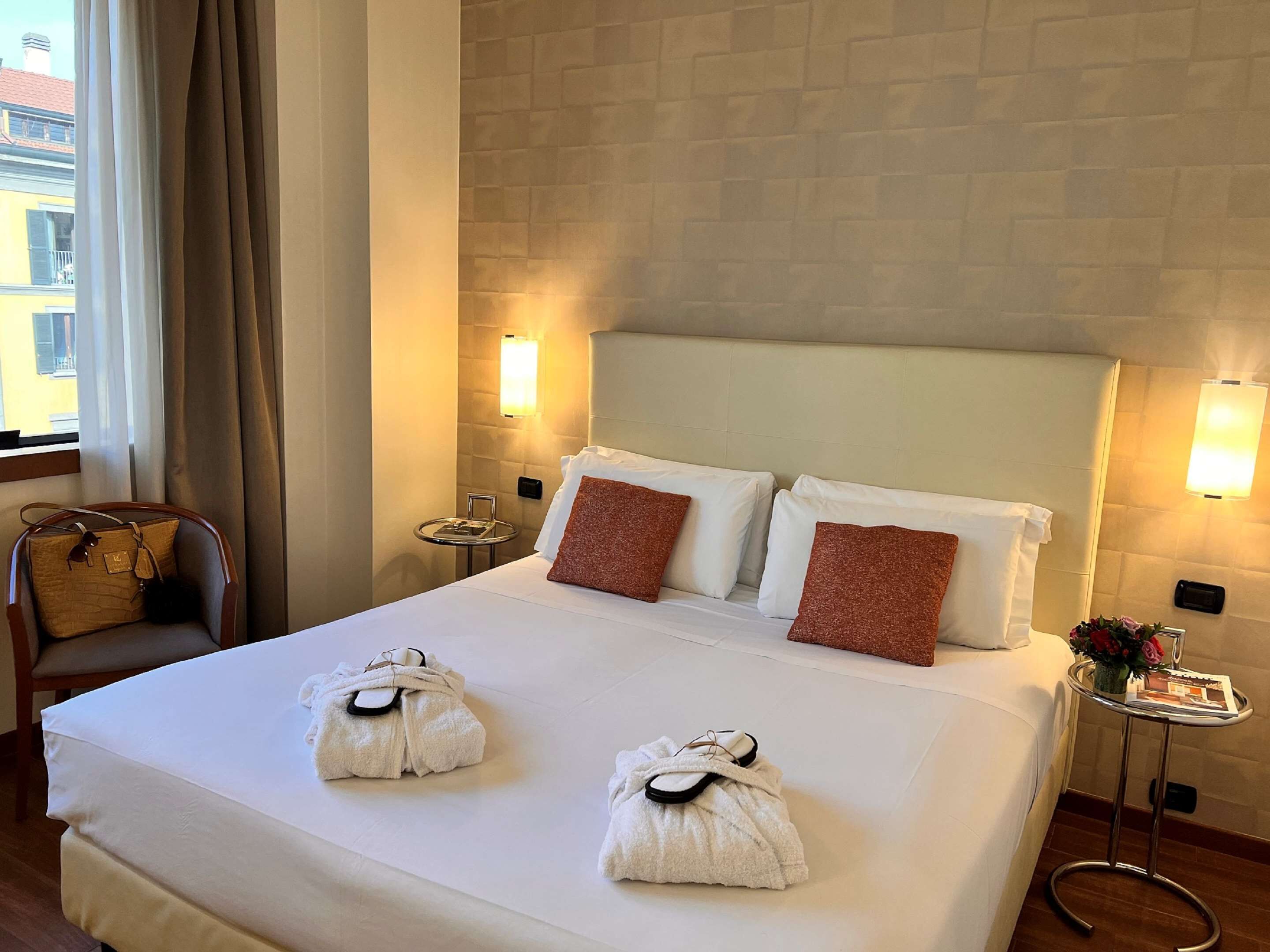 Una camera d'albergo con un letto grande, due cuscini, un comodino, una sedia e una finestra con tende.