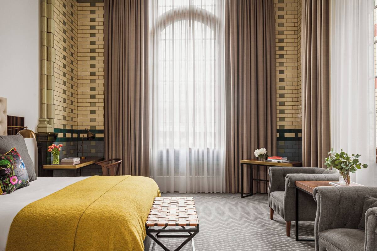 A hotel room with a large bed, a small table, a chair, and a sofa.