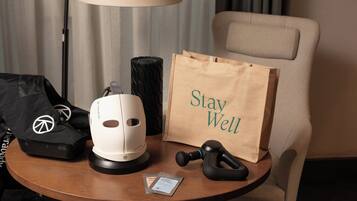 Une table sur laquelle se trouvent un fauteuil de massage, un appareil de massage blanc, un appareil de massage noir, un sac noir, un sac en papier marron avec l’inscription « Prenez soin de vous », et un petit paquet.