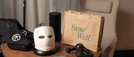 Une table sur laquelle se trouvent un fauteuil de massage, un appareil de massage blanc, un appareil de massage noir, un sac noir, un sac en papier marron avec l’inscription « Prenez soin de vous », et un petit paquet.
