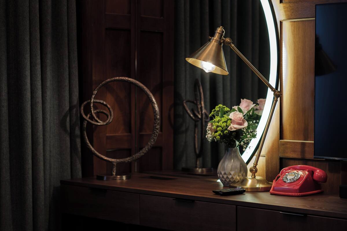 A desk with a vintage telephone, a desk lamp, and a vase with flowers.