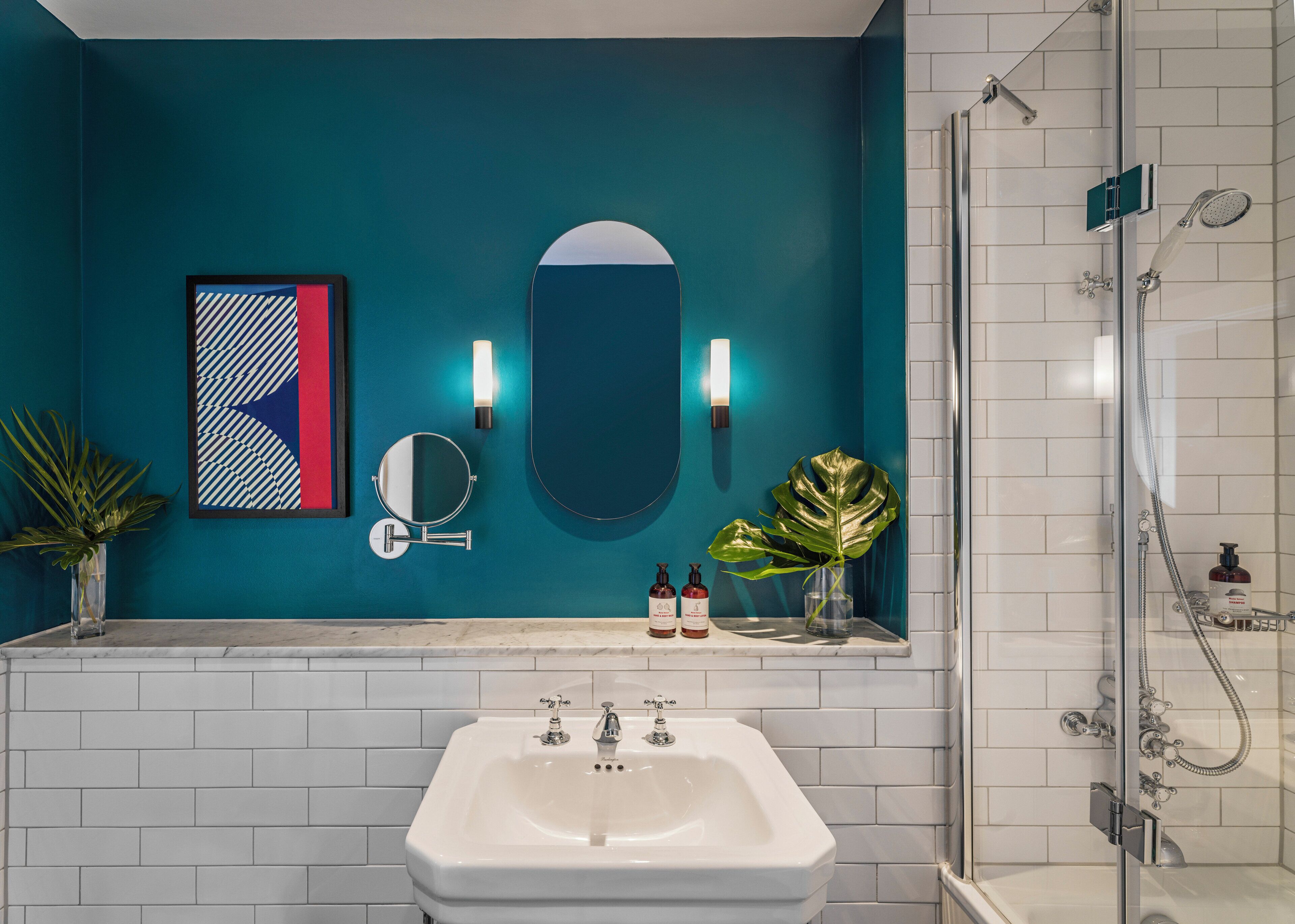 A bathroom with a white sink, a mirror, a round mirror, a shower, and a teal wall.